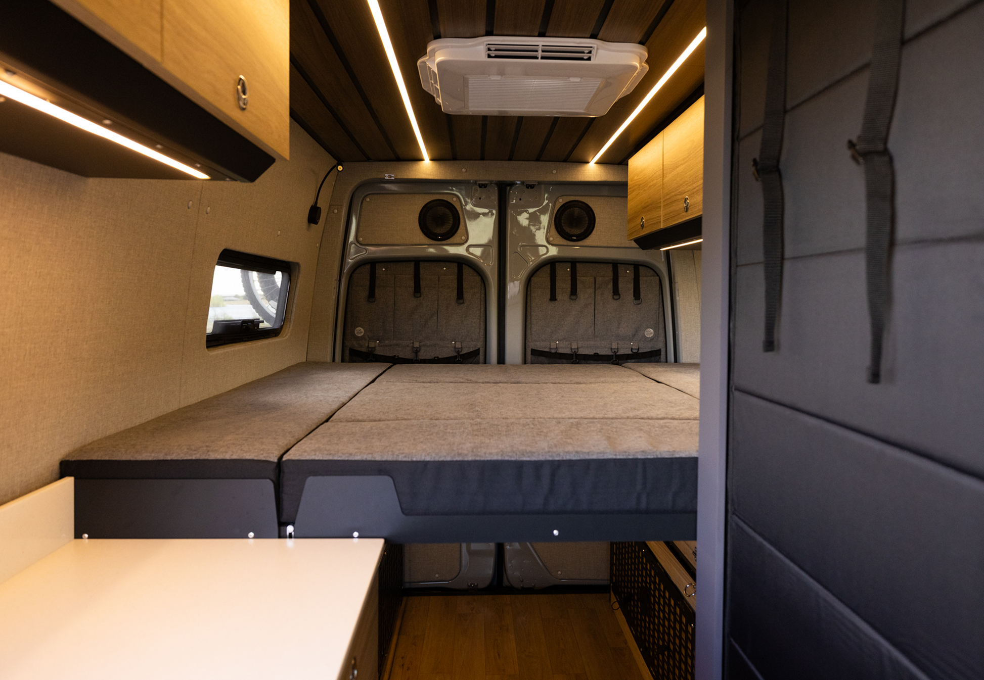 Sprinter van interior with Highland Vans Murphy Bed System extended into full sleeping position, warm wood and LED lighting